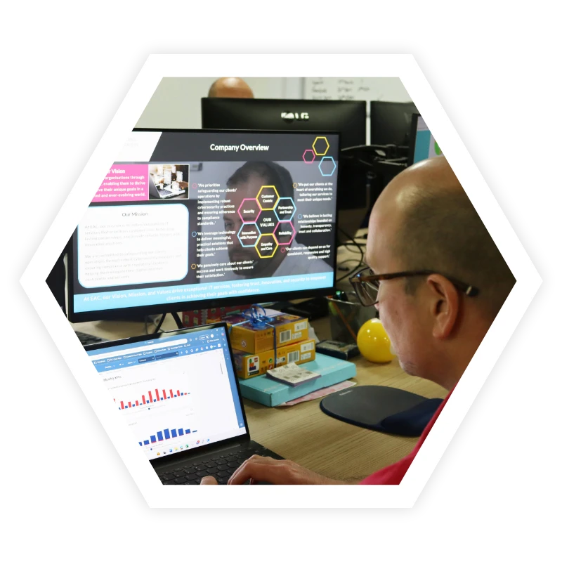 Man using laptop at desk with computer screens displaying company overview documents
