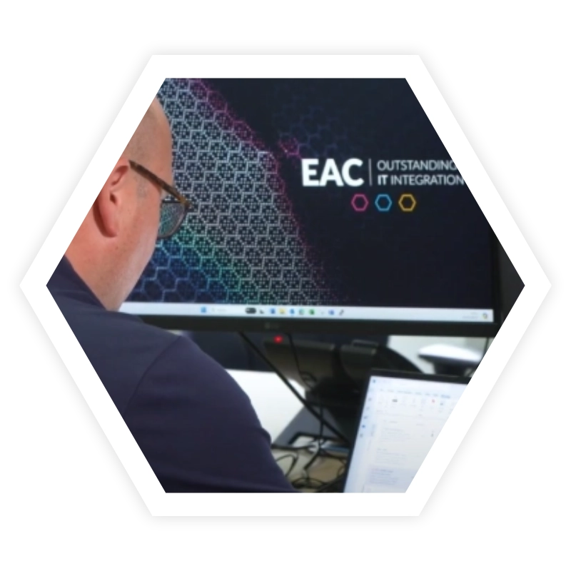 Ben typing on laptop connected to two monitors with EAC wallpaper and