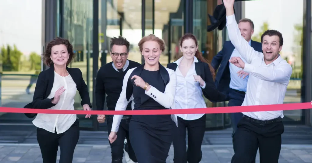 Team of people running through red ribbon